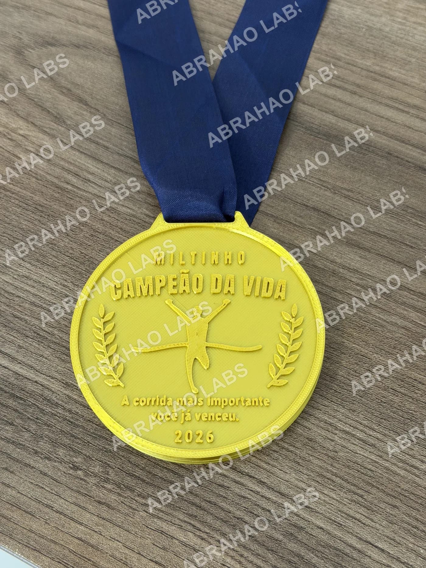 Foto real da medalha de homenagem Campeão da Vida impressa em 3D, dourada com fita azul, corredor e louros em relevo